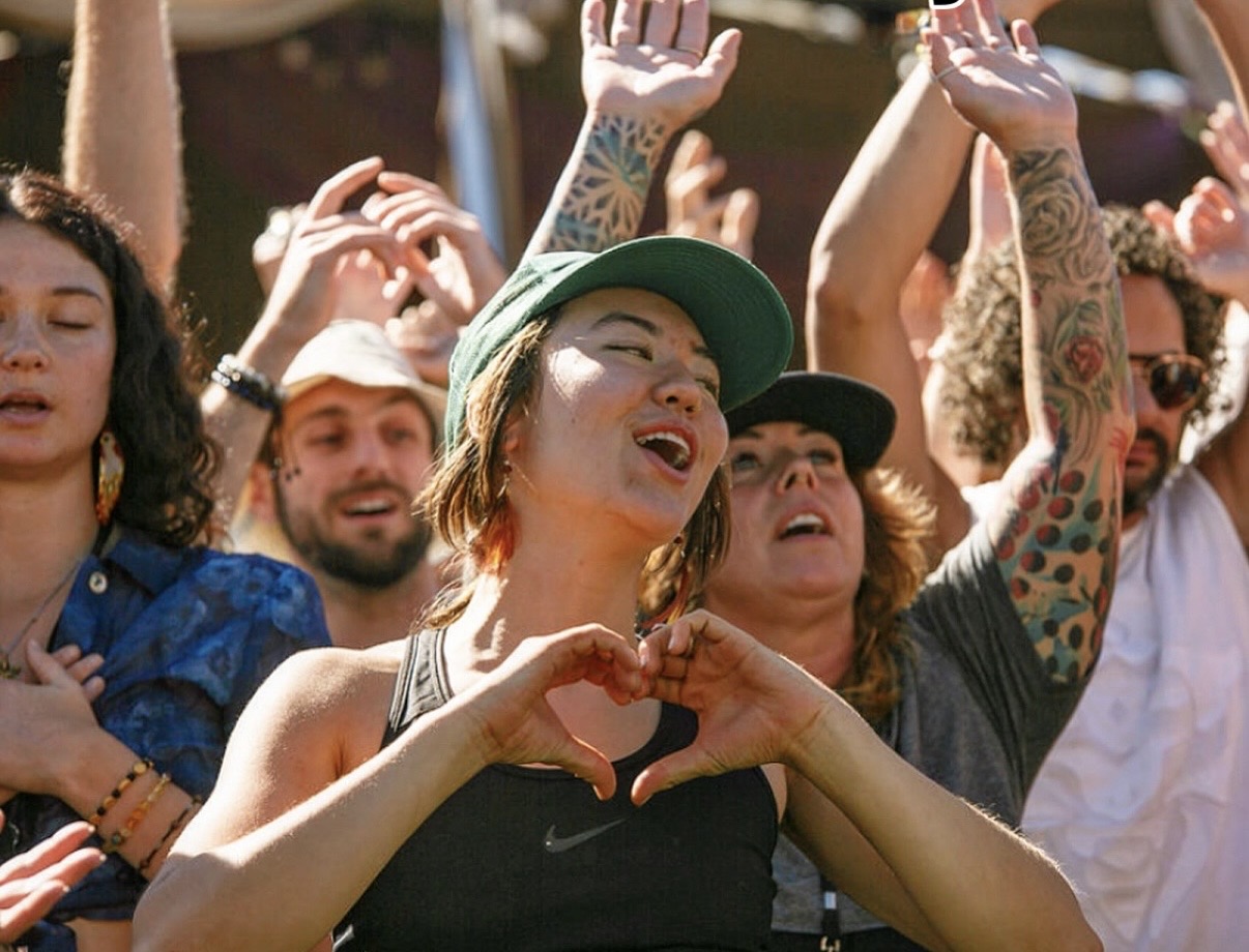 Angela in the crowd at a festival, making a heart with her hands